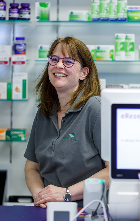 Apothekerin der Martinus Apotheke steht hinter dem Tresen vor dem Medikamentenregal.