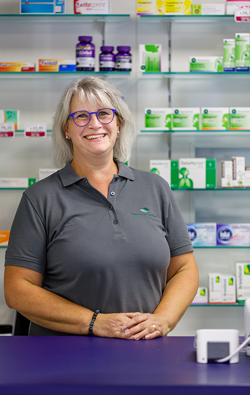 Apothekerin der Martinus Apotheke steht hinter dem Tresen vor dem Medikamentenregal.