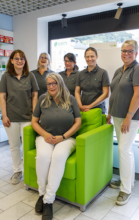 Das Team der Martinus Apotheke in Trier steht un einen grünen Sessel in dem eine Apothekerin sitzt.