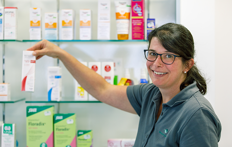 Apothekerin der Martinus Apotheke steht vor einem Medikamentenregal und hält ein Medikament in der Hand.