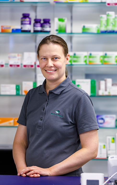 Apothekerin der Martinus Apotheke steht hinter dem Tresen vor dem Medikamentenregal.