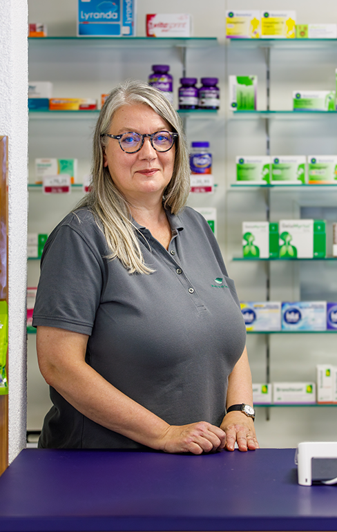 Apothekerin der Martinus Apotheke steht hinter dem Tresen vor dem Medikamentenregal.