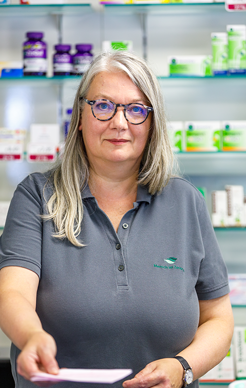 Apothekerin der Martinus Apotheke steht mit einer Broschüre, hinter dem Tresen, vor dem Medikamentenregal.