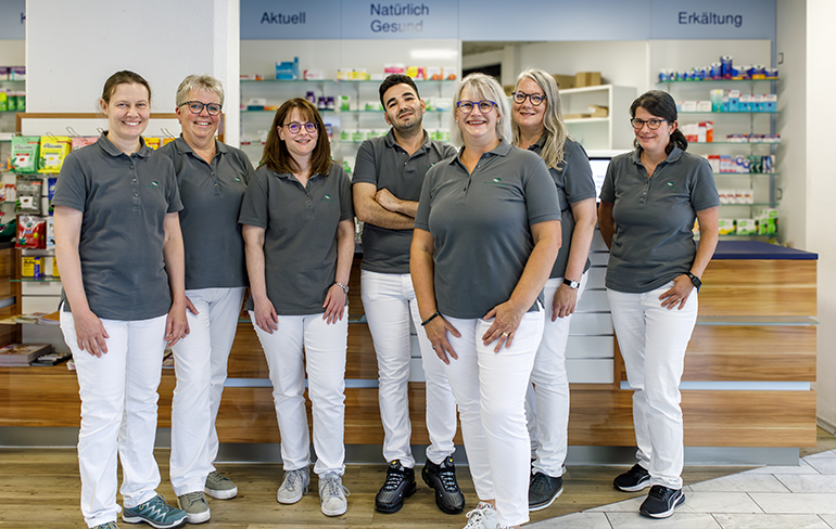 Das Team der Martinus Apotheke in Trier steht zusammen in der Apotheke, im Hintergrund stehen Medikamentenregale.