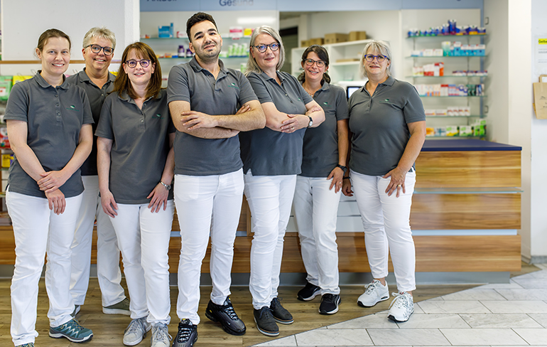 Das Apothekenteam steht vor dem Tresen in der Martinus Apotheke, im Hintergrund ist der Tresen.