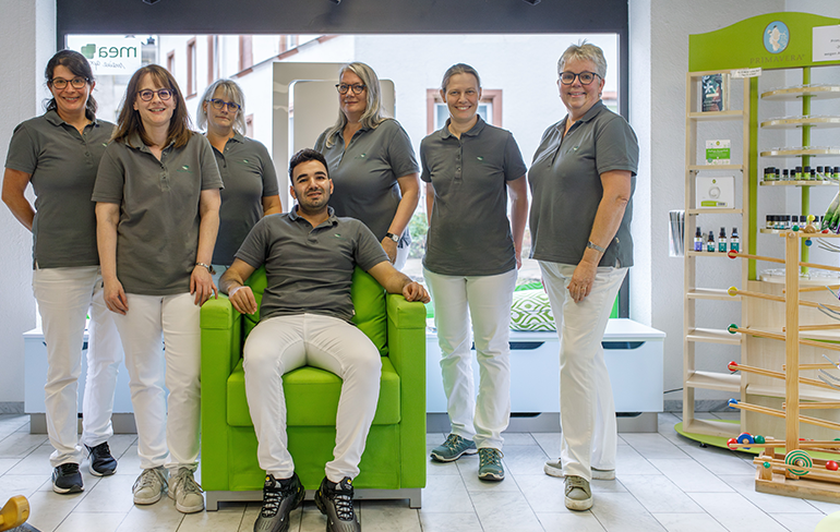 Das Team der Martinus Apotheke in Trier steht un den sitzenden Inhaber der Apotheke, der in einem grünen Sessel von dem Fenster sitzt.