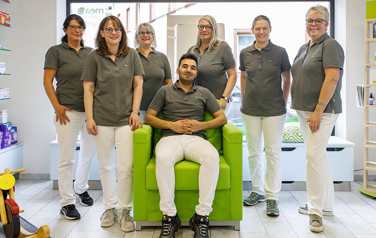 Das Team der Martinus Apotheke in Trier steht un den sitzenden Inhaber der Apotheke, im Hintergrund ist ein Fenster.