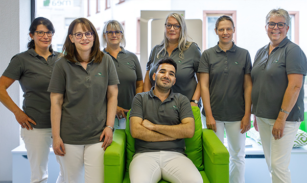 Das Team der Martinus Apotheke in Trier steht un den sitzenden Inhaber der Apotheke vor dem Fenster.