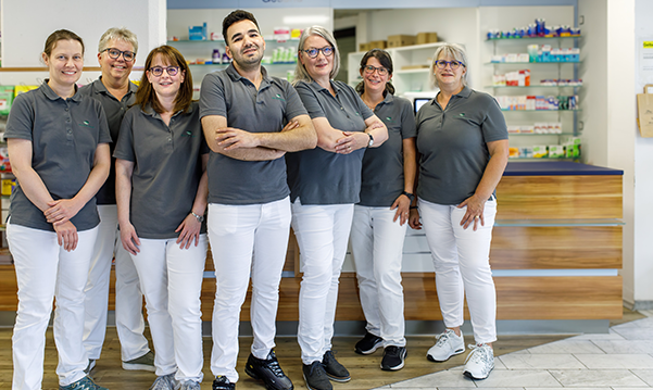 Das Team der Martinus Apotheke steht in der Apotheke vor den Medikamentenregalen.