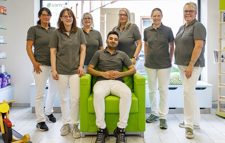 Das Team der Martinus Apotheke in Trier steht in der Apotheke von den Medikamentenregalen.
